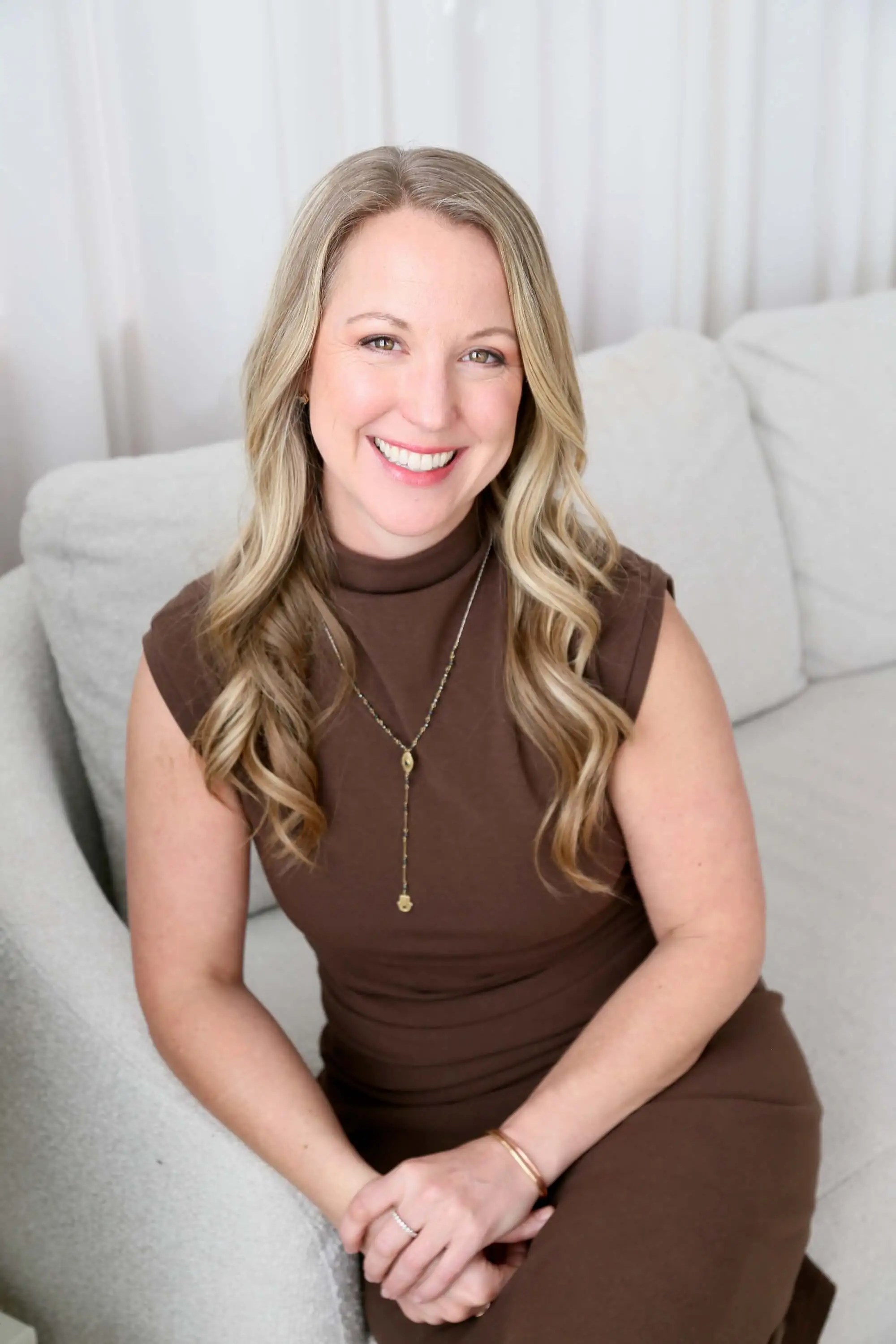 Emily Wishall, somatic coach and Certified Rolfer®, smiling while seated on a couch,  smiling while seated on a couch.